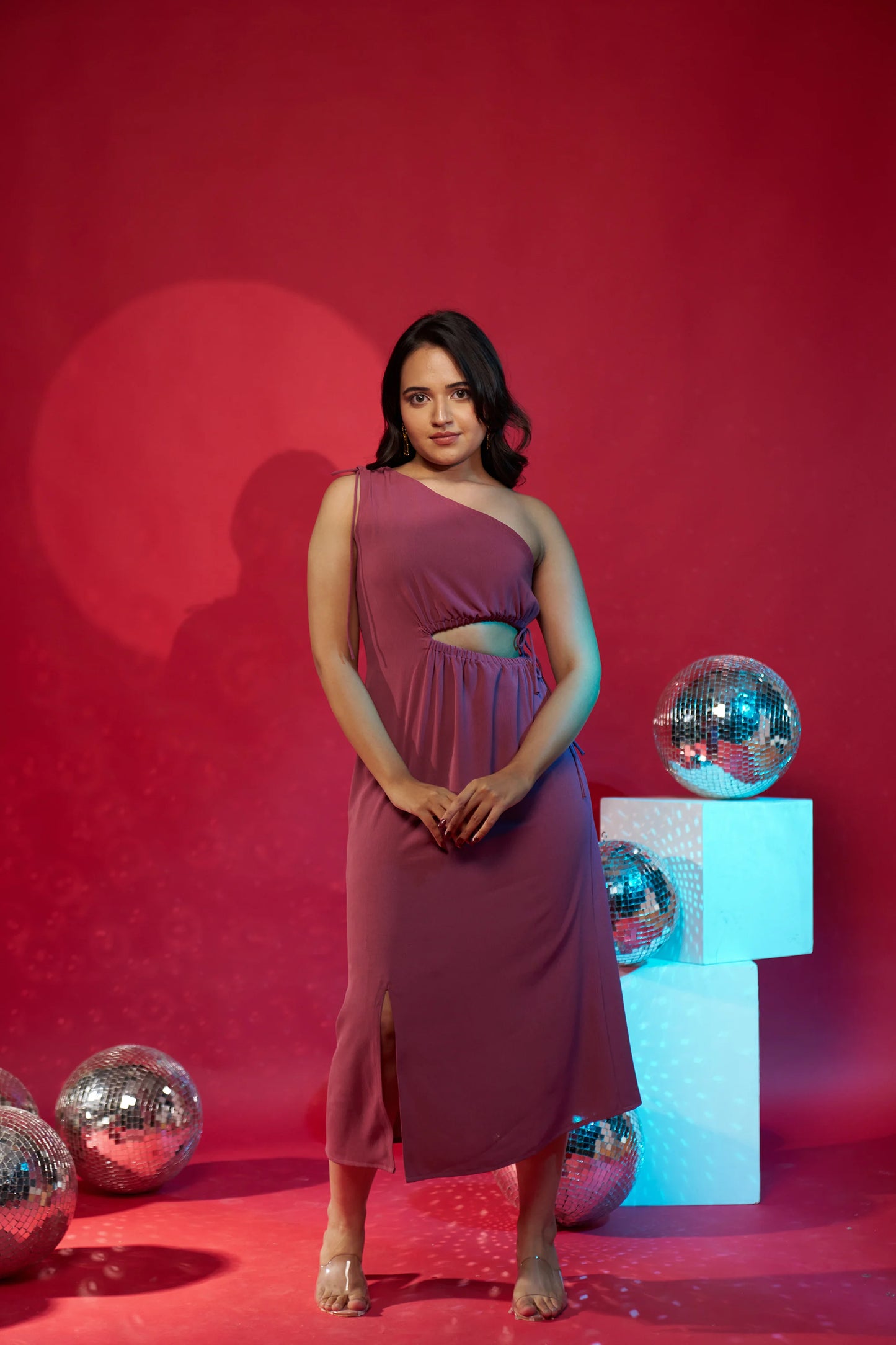 Woman in a pink dress standing against a red background with disco balls.