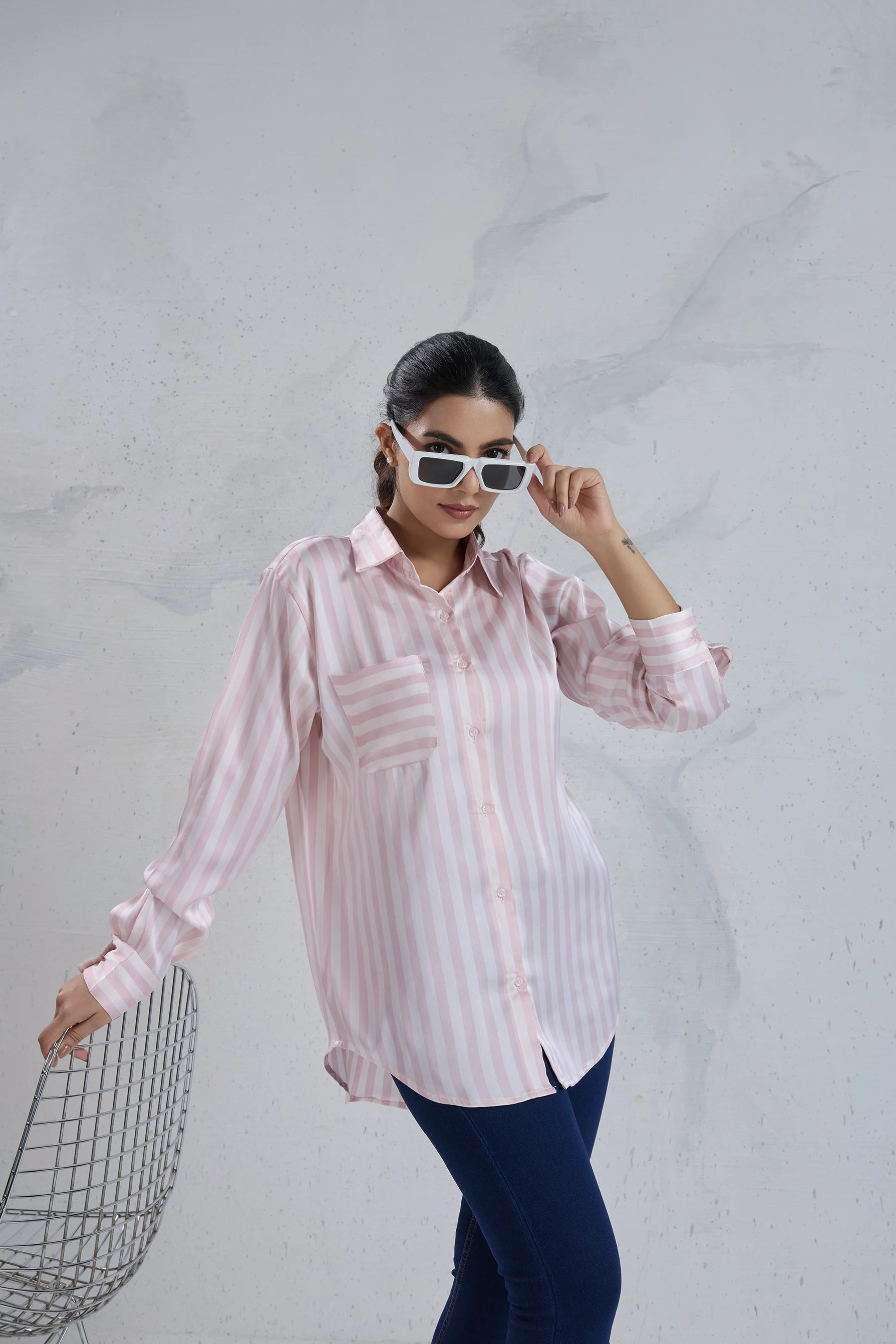 Woman wearing a striped shirt and sunglasses against a textured white wall