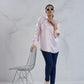 Person wearing a light pink shirt and dark blue jeans standing next to a wire chair against a white background