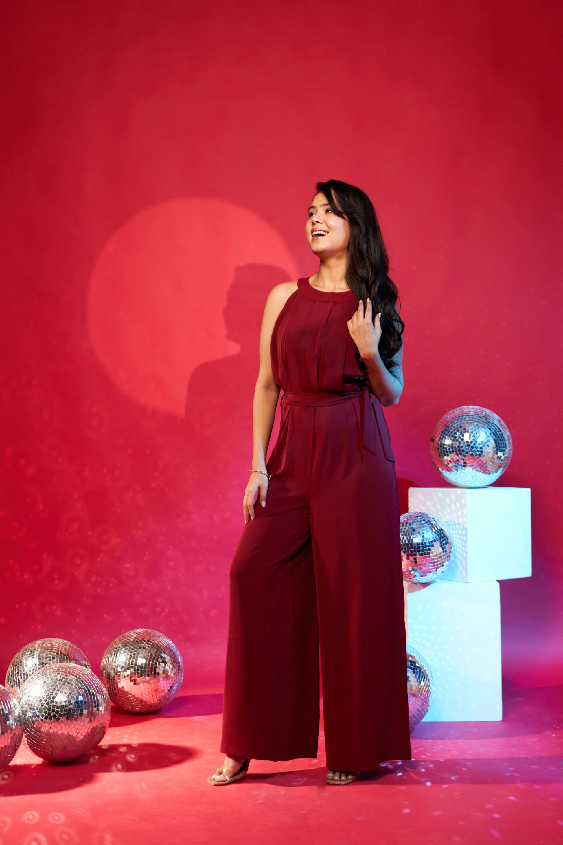 Woman in a red jumpsuit standing against a red background with decorative spheres.