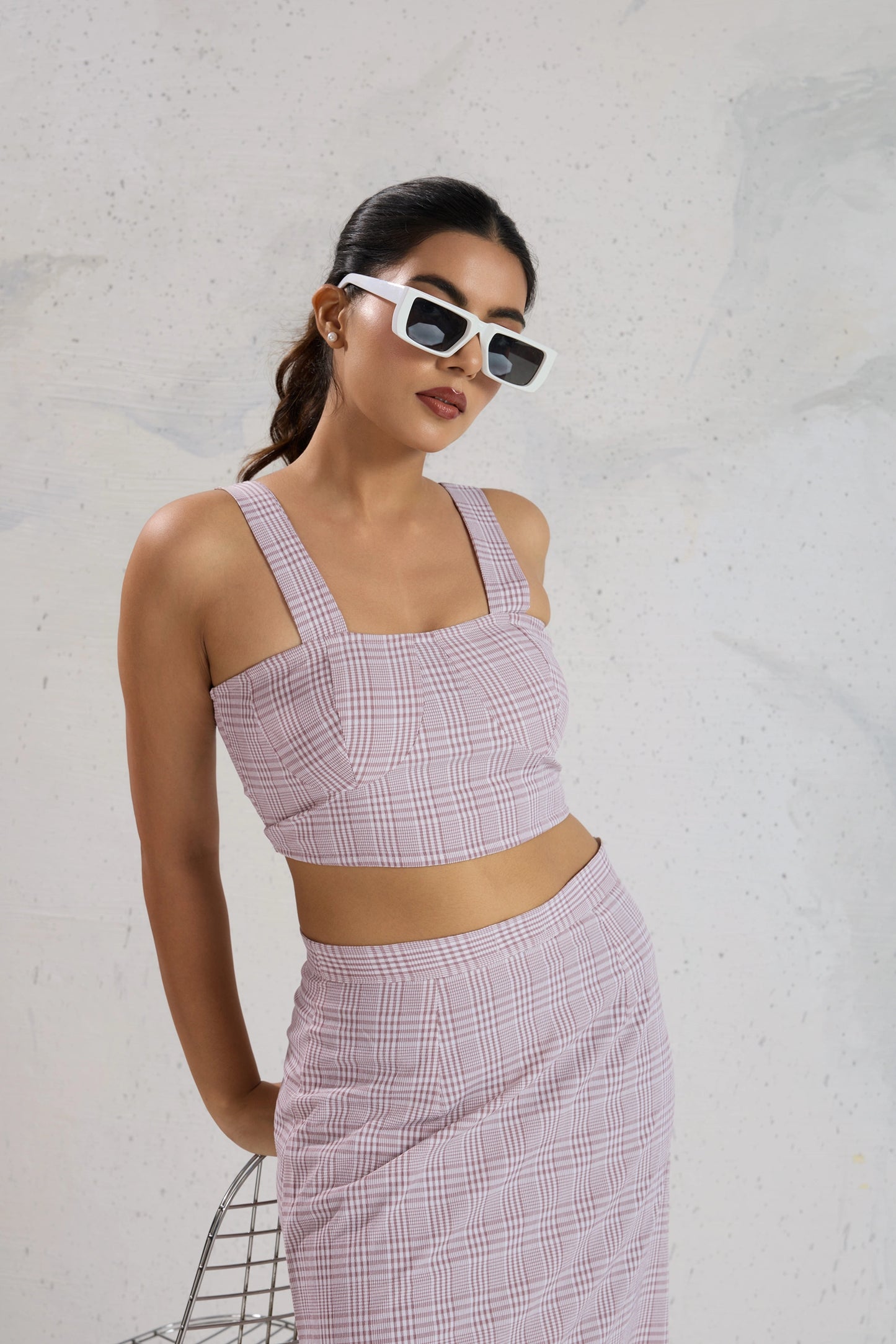 Woman wearing a pink checkered outfit with sunglasses against a light gray background