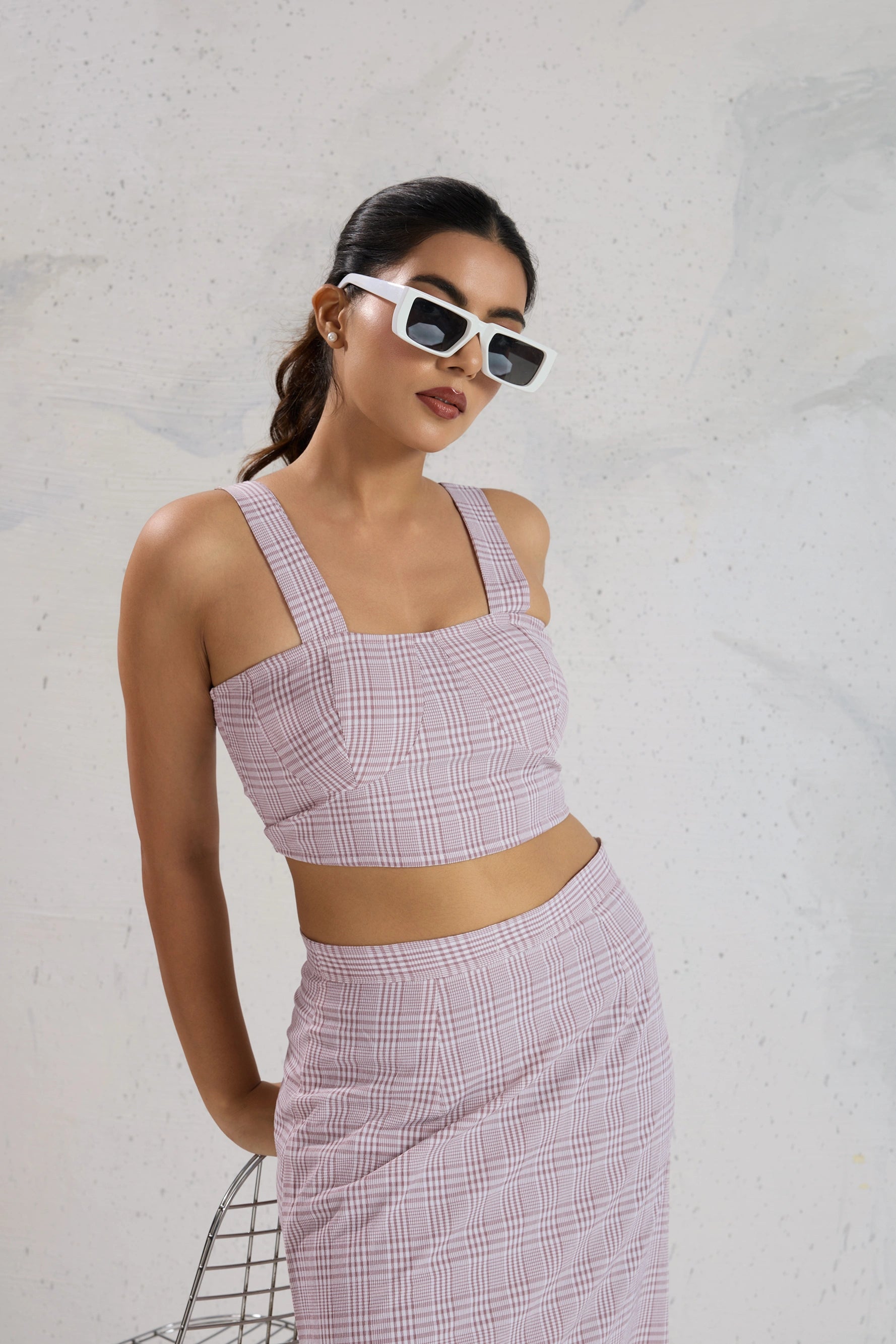 Woman wearing a pink checkered outfit with sunglasses against a light gray background