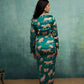 Woman wearing a teal dress with animal pattern against a textured green wall.