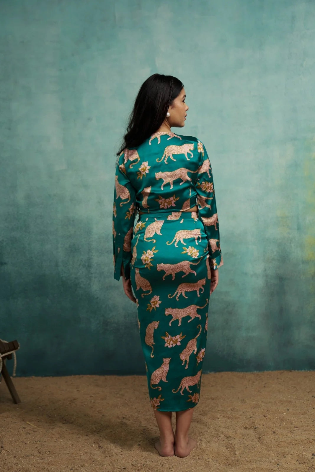 Woman wearing a teal dress with animal pattern against a textured green wall.
