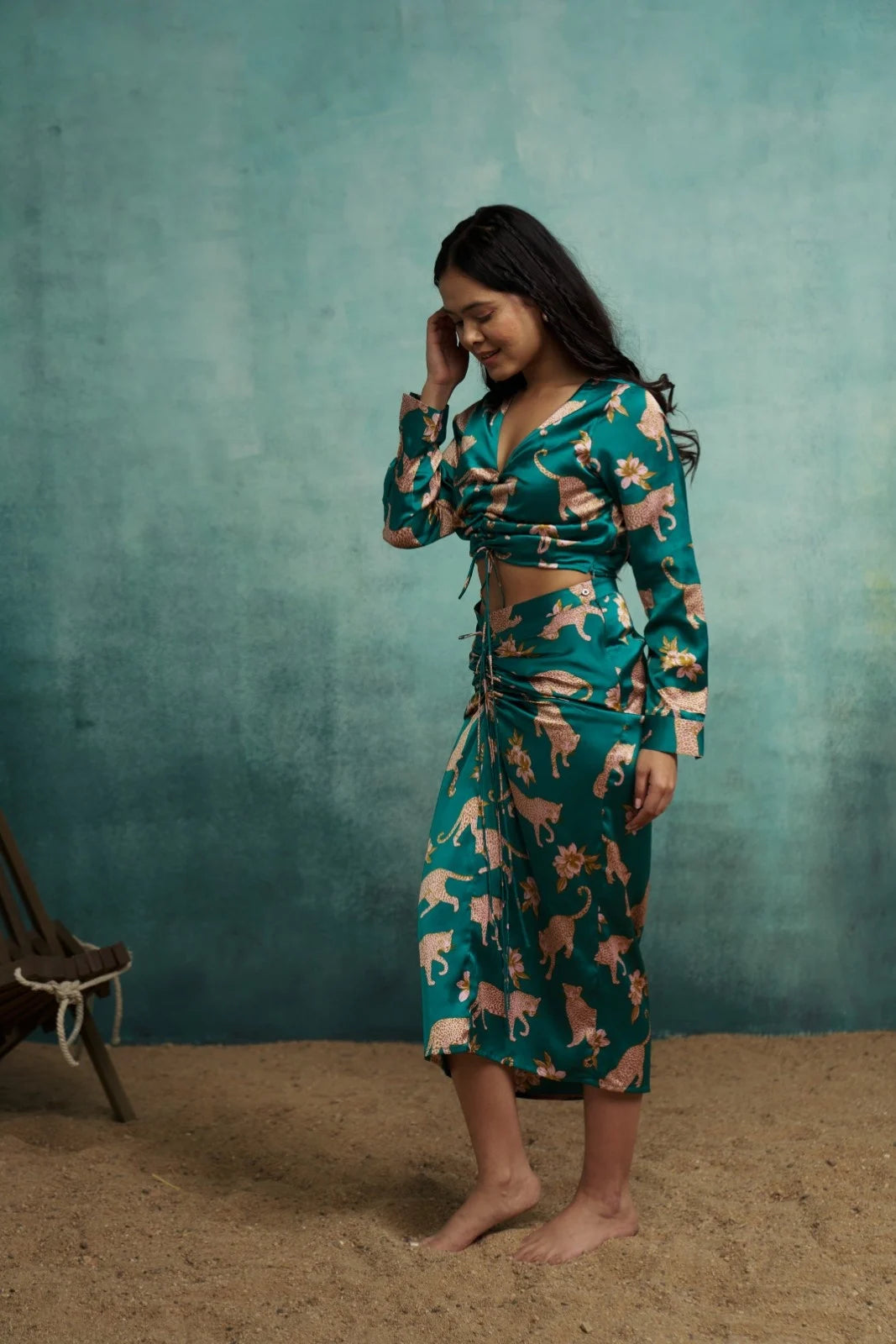Woman wearing a teal patterned outfit against a textured green wall.
