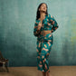 Woman wearing a green patterned outfit against a textured teal wall.