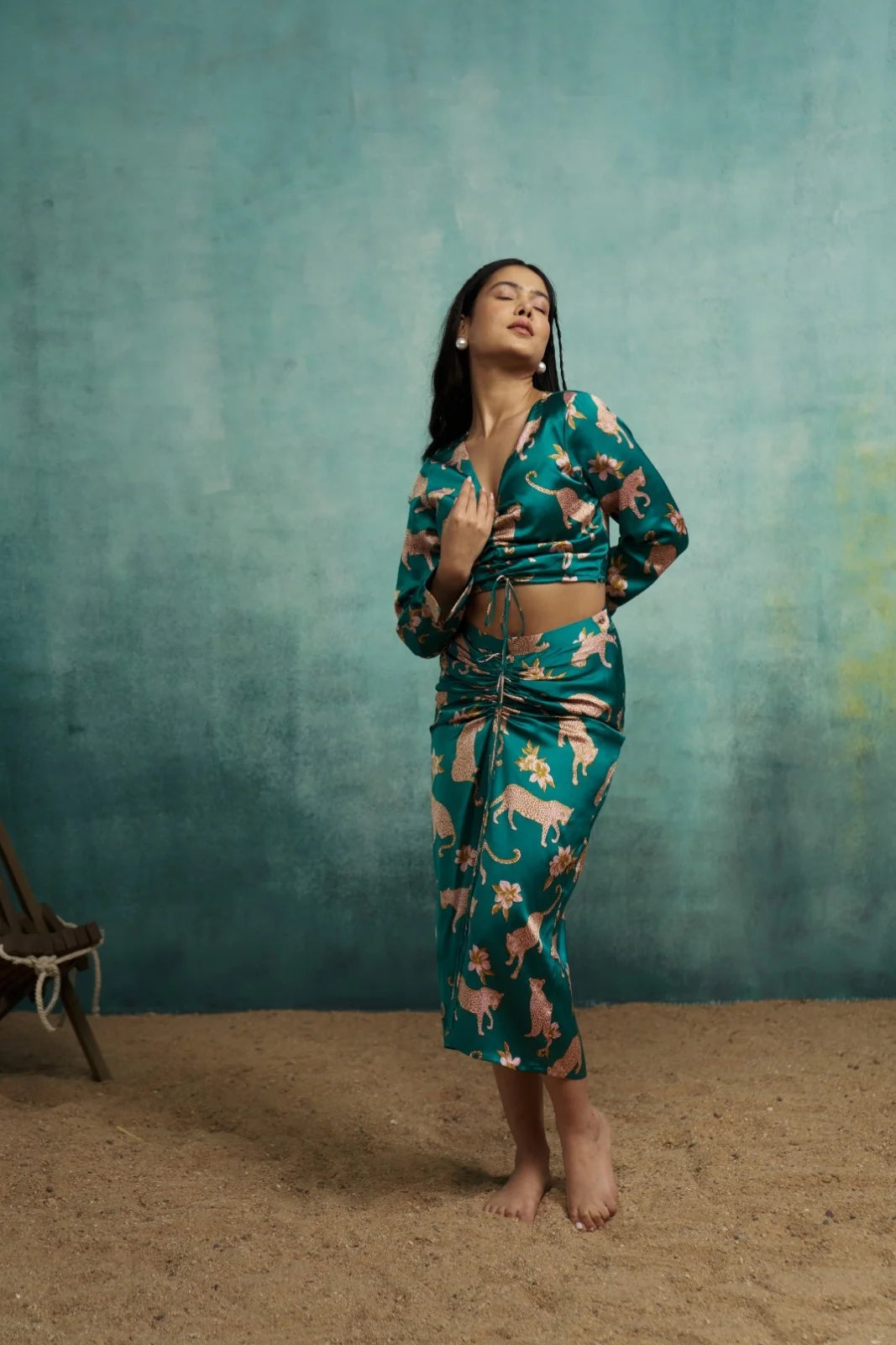 Woman wearing a green patterned outfit against a textured teal wall.