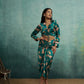 Woman wearing a patterned outfit against a textured teal wall.