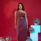 Woman in a burgundy dress standing against a red background with reflective silver spheres.