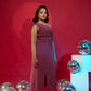 Woman in a pink dress standing against a red background with reflective silver spheres.