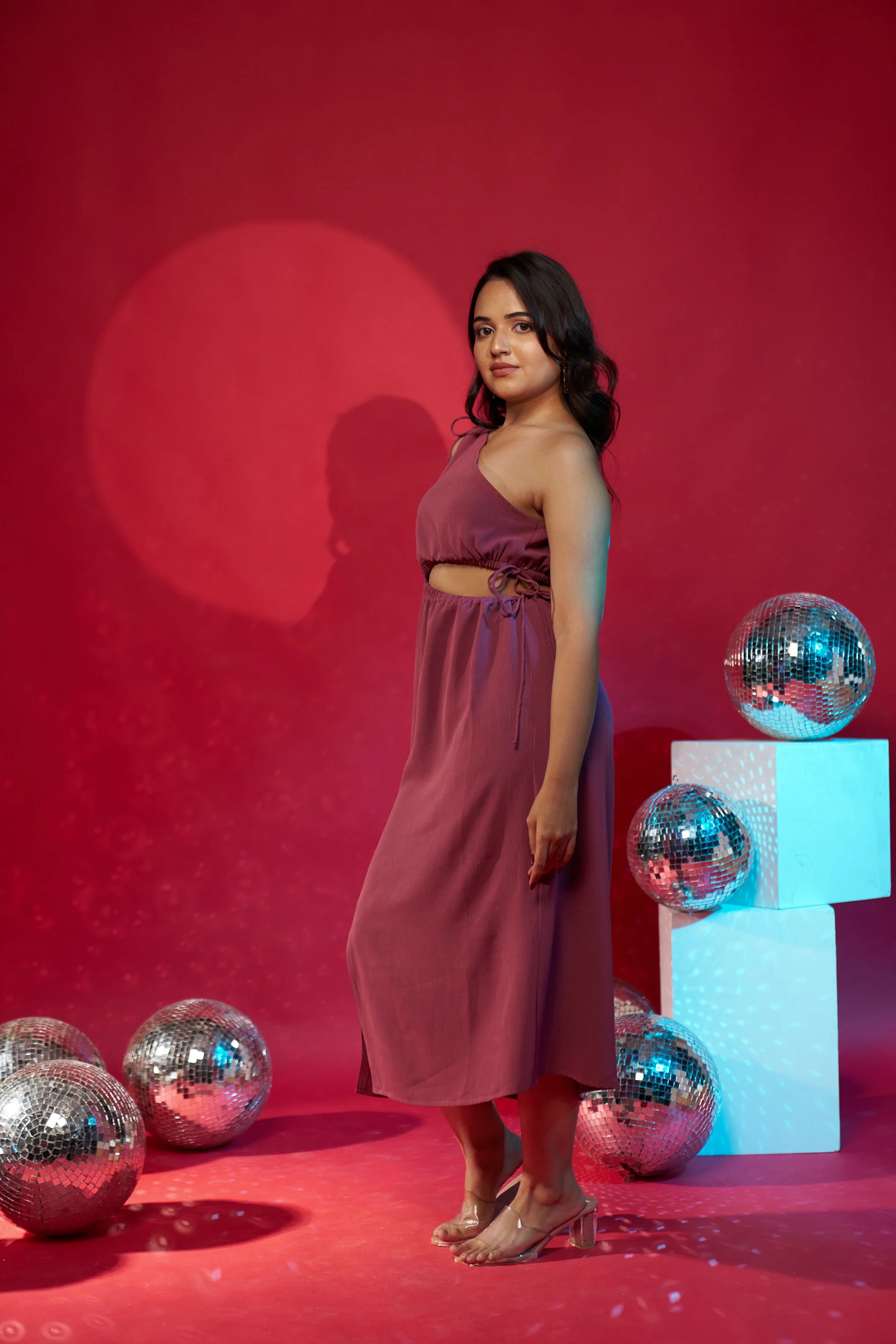 Woman in a pink dress standing against a red background with disco balls.