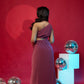 Woman in a burgundy dress standing in front of a red wall with disco balls.