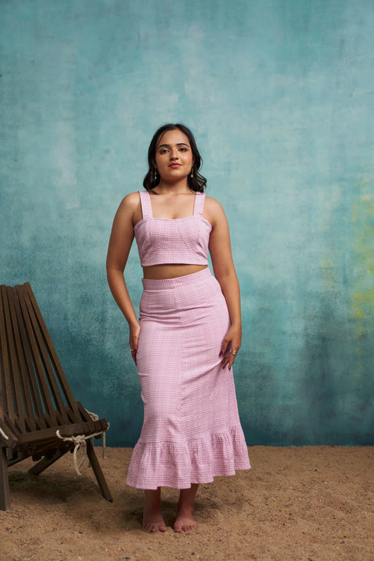Woman in a pink outfit standing against a textured blue wall with a wooden chair.