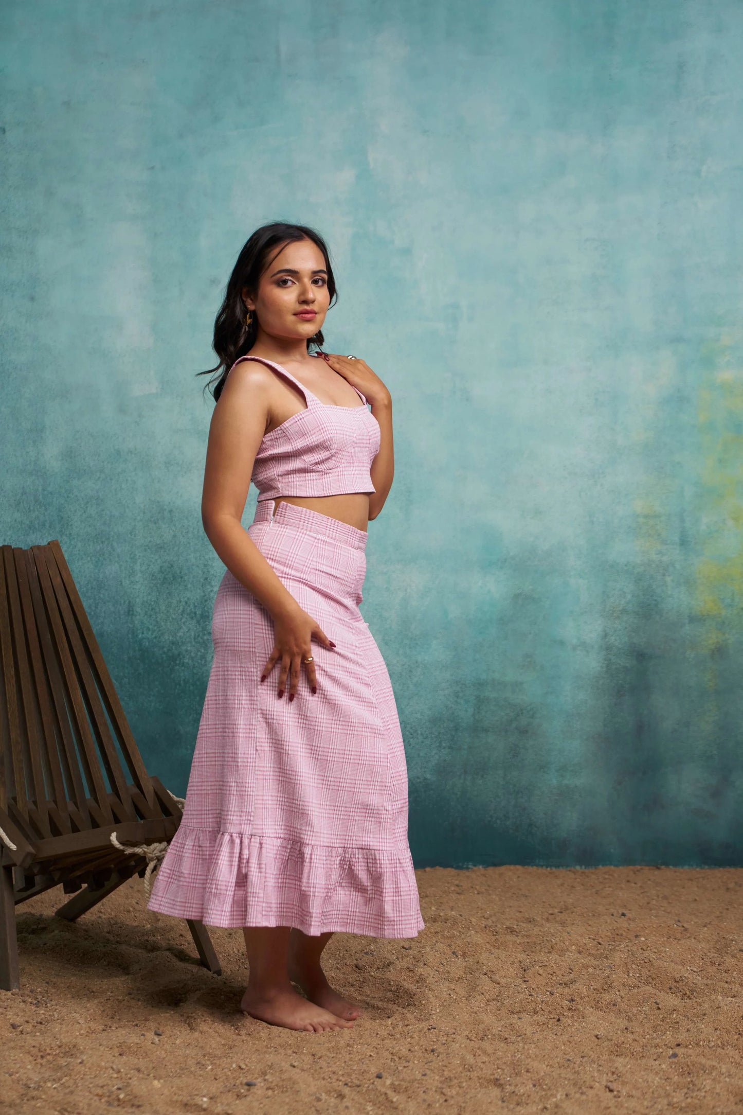 Woman in a pink outfit standing against a textured blue wall.