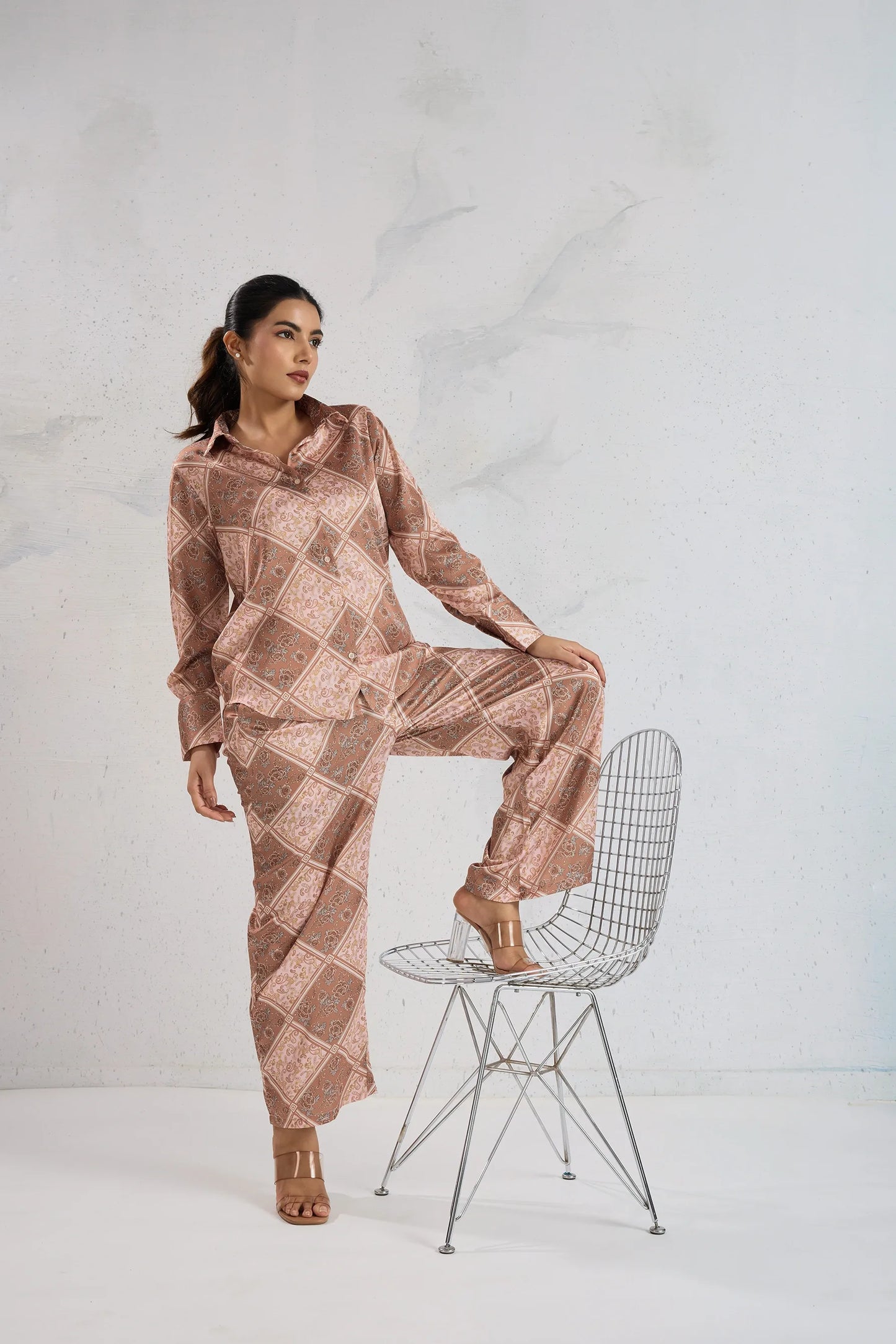 Woman in a patterned outfit sitting on a wire chair against a white background