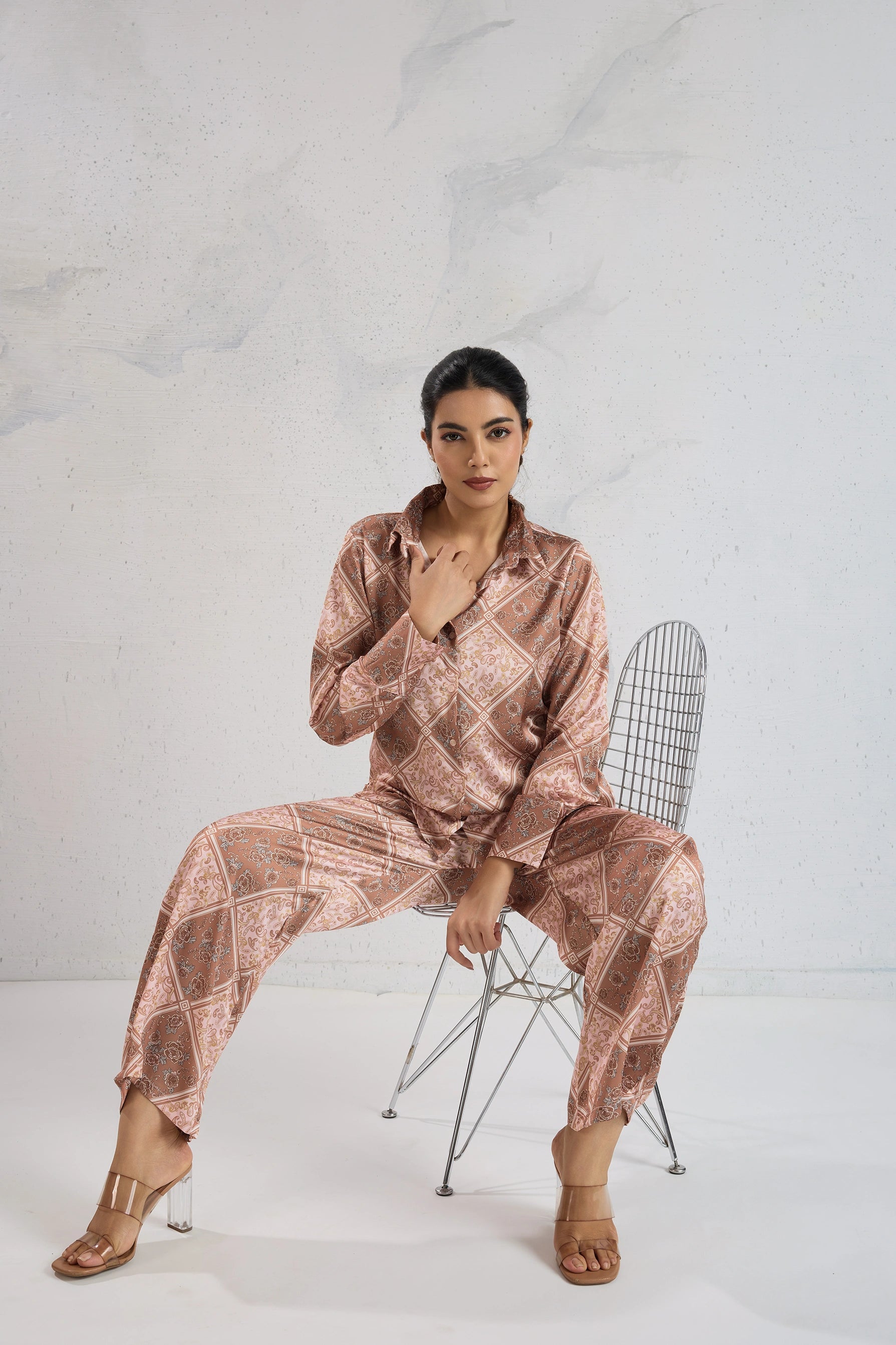 Woman in a patterned outfit sitting on a chair against a white background