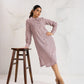Woman in a pink dress standing next to a wooden stool on a white background