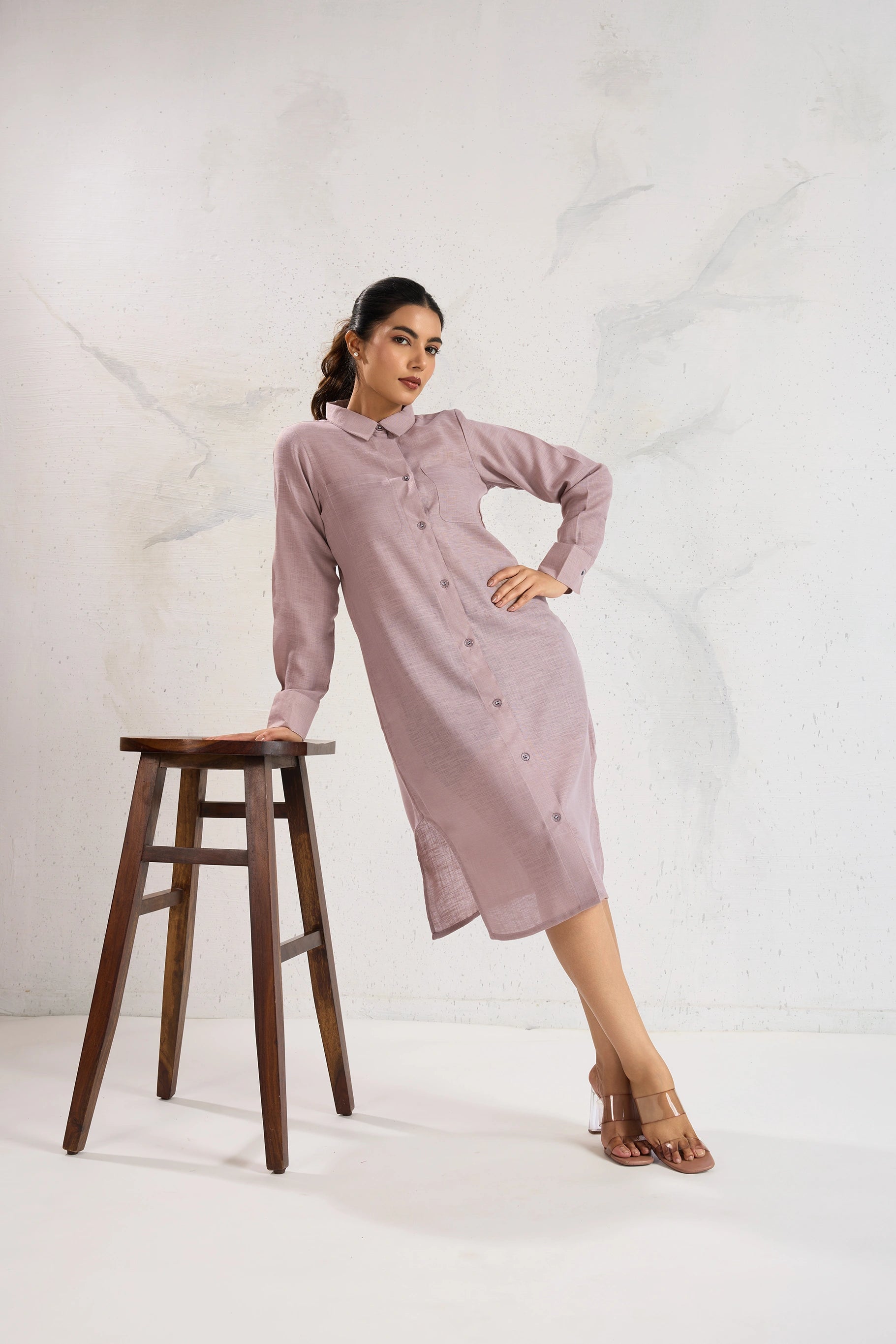 Woman in a pink dress standing next to a wooden stool on a white background