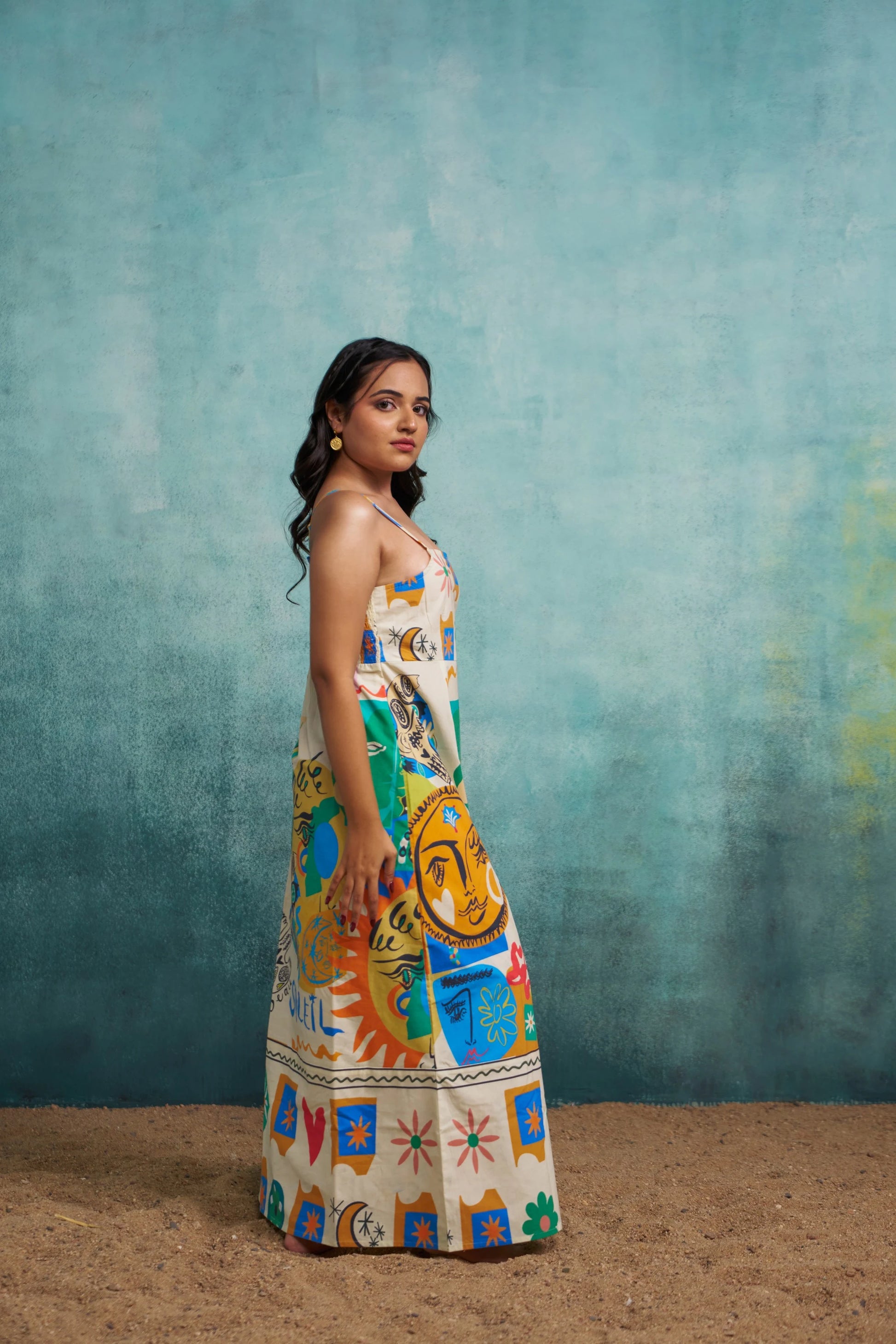 Woman wearing a colorful dress with artistic designs against a textured blue wall.