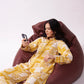 Woman in yellow and white patterned outfit sitting on a brown bean bag chair, using a phone.