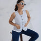 Woman sitting on a stool wearing a sleeveless top and jeans against a white background