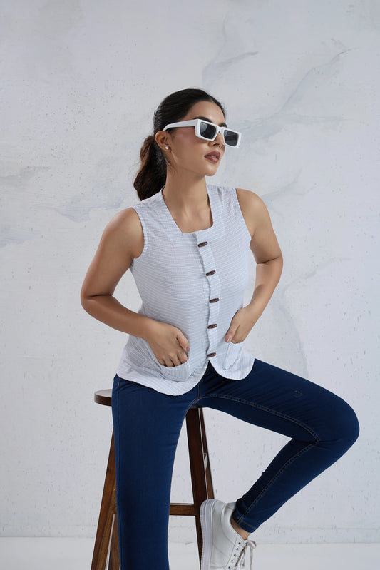Woman sitting on a stool wearing a sleeveless top and jeans against a white background