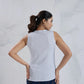 Woman wearing a sleeveless white top and blue jeans against a light gray background