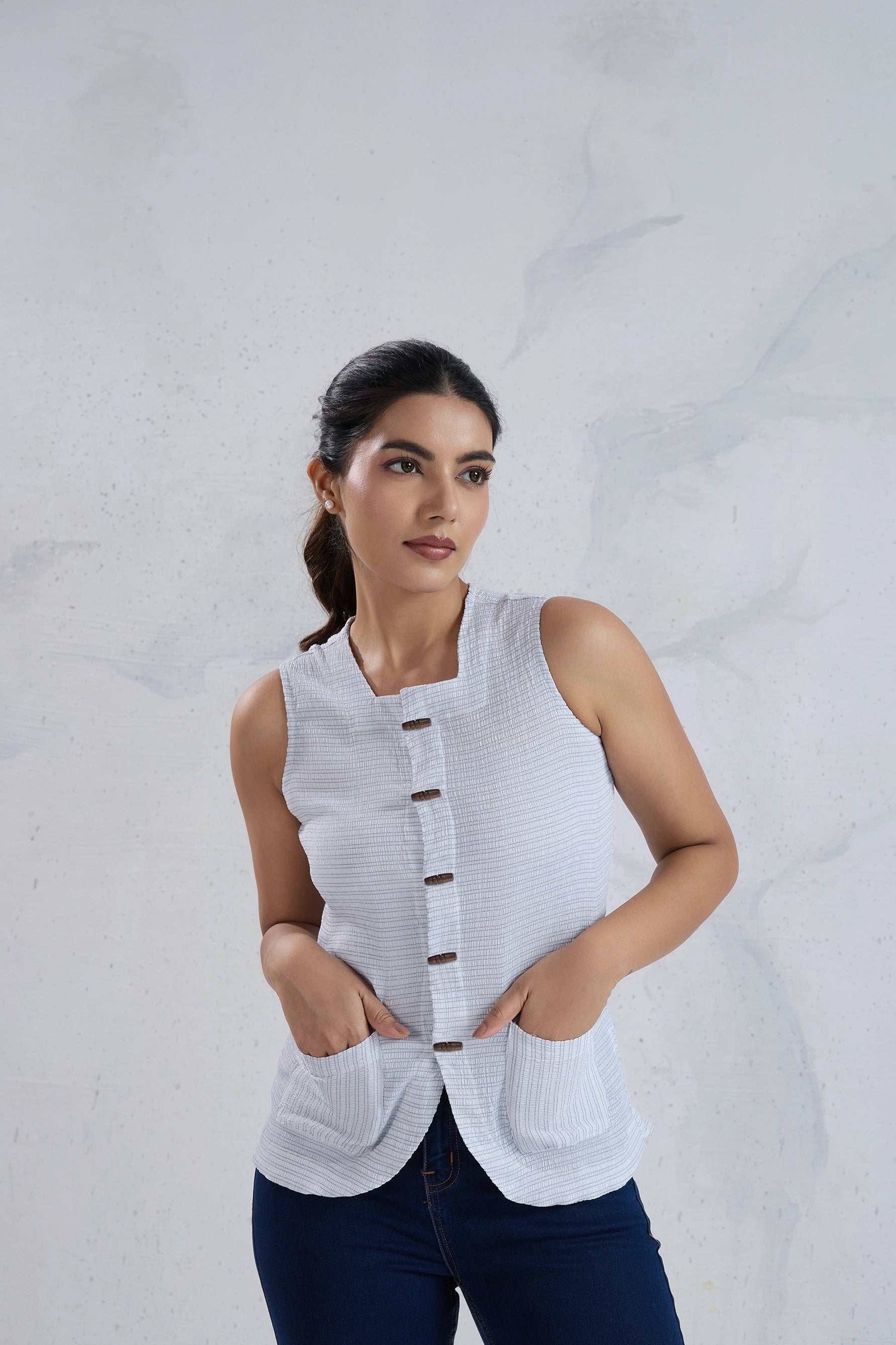 Woman wearing a white sleeveless knitted top against a light gray background